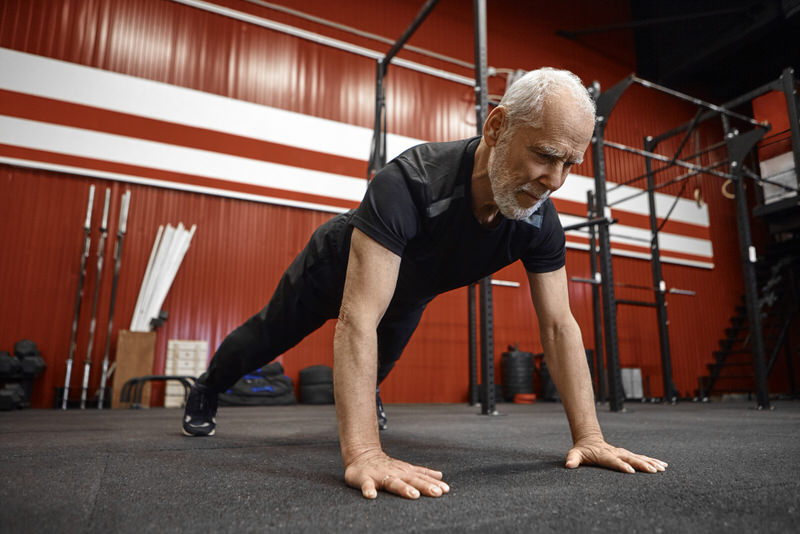 An man in is 60s is committed to working out and staying fit, and is doing some pushups to build endurance and strength.