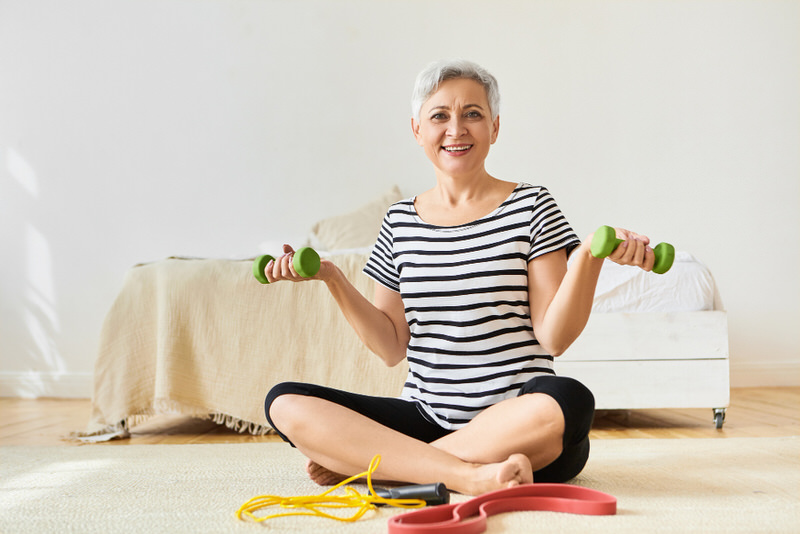 A woman in her 60s is on the ground reviewing her workout equipment, so she can start working out and build her strength safely and gradually.
