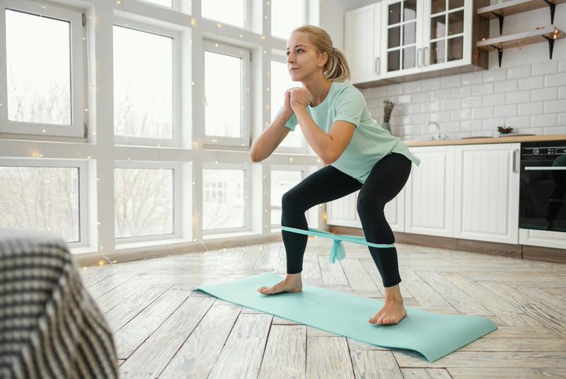 A young woman in her 50s is on a yoga mat, doing resistance band exercises to build her core.
