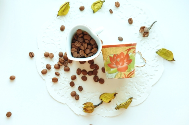 Coffee beans in a cup, and scattered on a table.