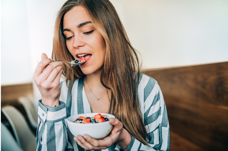 A young woman is eating a small bowl of oatmeal as her pre-workout meal. A light and wholesome meal will help her get energy without feeling bloated and nauseous.