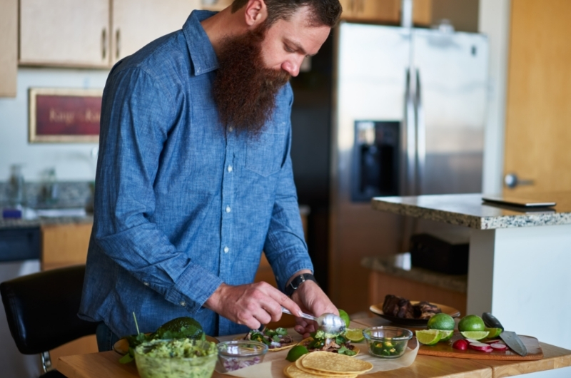 A young man is making tacos with guacamole for his healthy dinner.