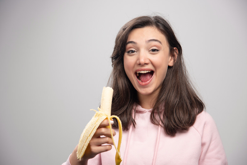 A young woman is eating a banana and smiling.
