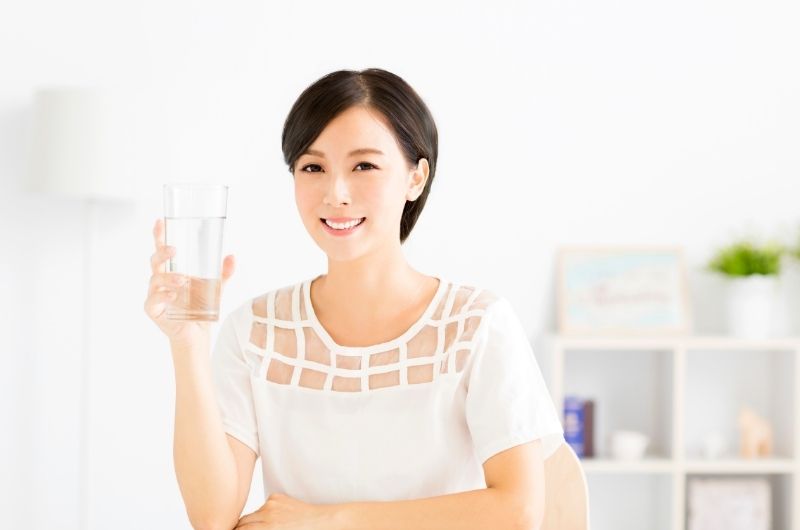 A young woman is drinking water slowly while sitting down to help prevent any stomach pain