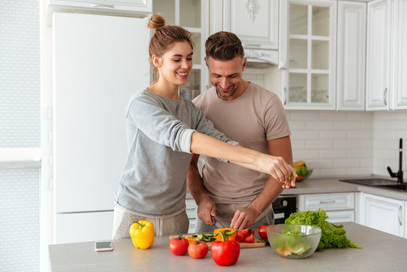 A young couple is preparing a healthy salad together as part of their safe and healthy low-calorie diet.