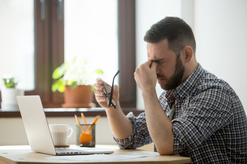 A young man is stressed out from working and is getting a pulsating feeling from below his eyes.