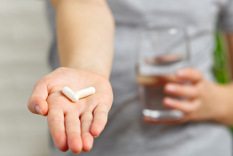 A young woman is holding out 2 vitamins on her palm, double the amount of what her recommended daily dosage is.