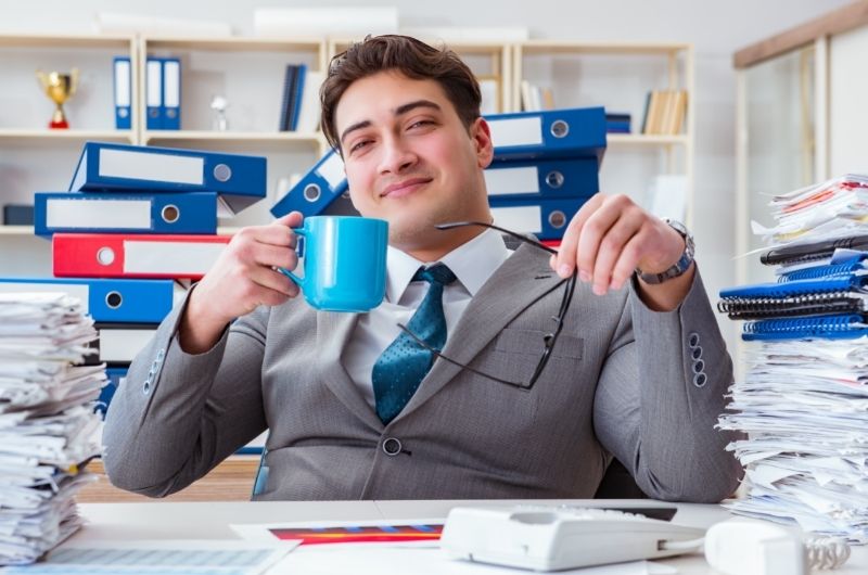 A young man is working at the office, overwhelmed with the amount of work, and is drinking too much coffee in one day.