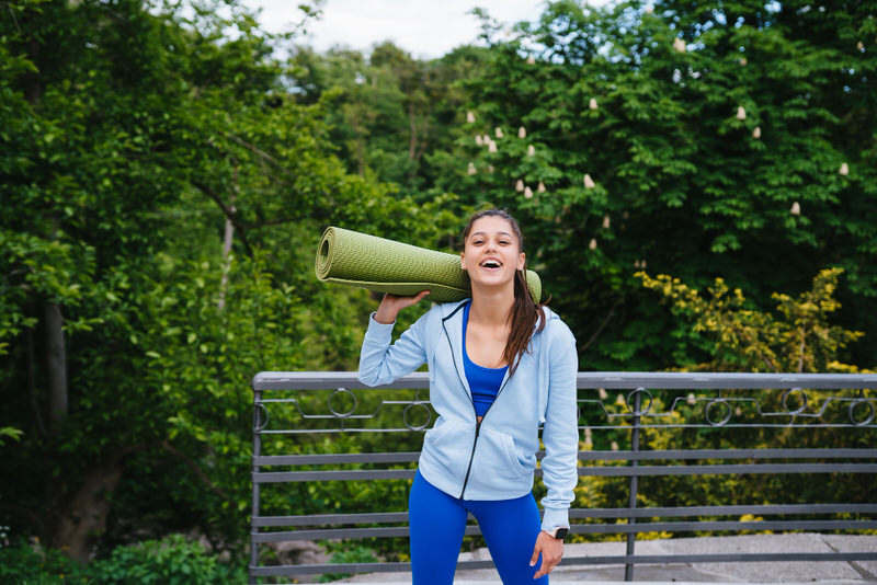 A young woman is holding her yoga mat and is ready to do some yoga outside.