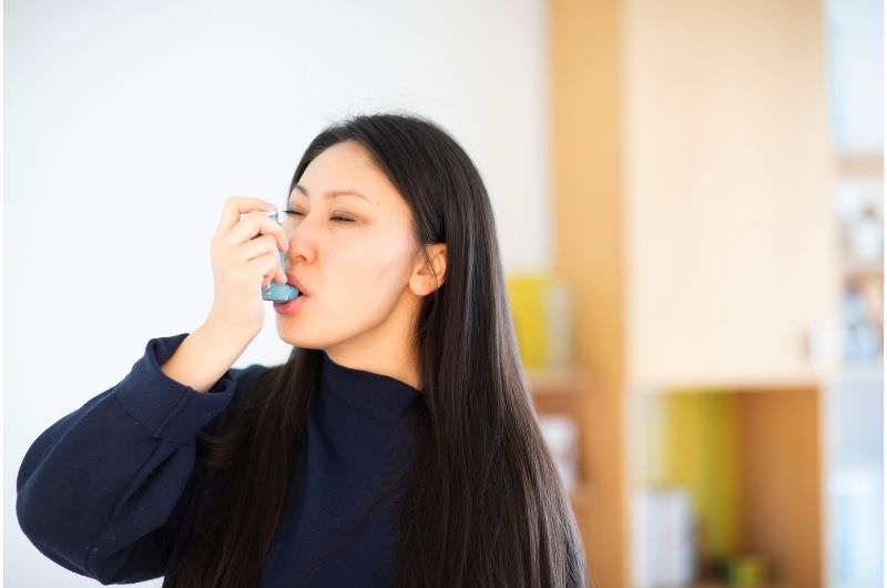 A woman is using an asthma inhaler after struggling to breathe in the cold air.