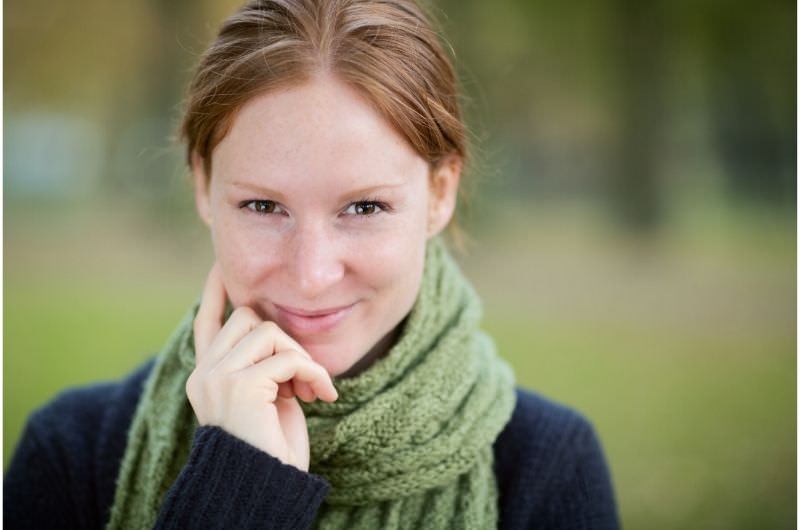A young woman is wearing a scarf to avoid getting cold.