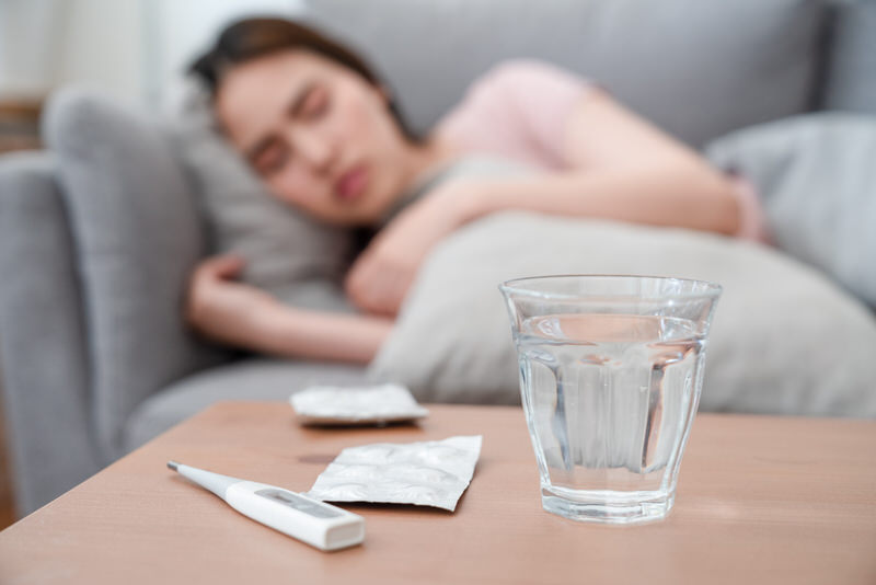 A young woman is laying down on the sofa after taking some medication for her recurring strep throat.