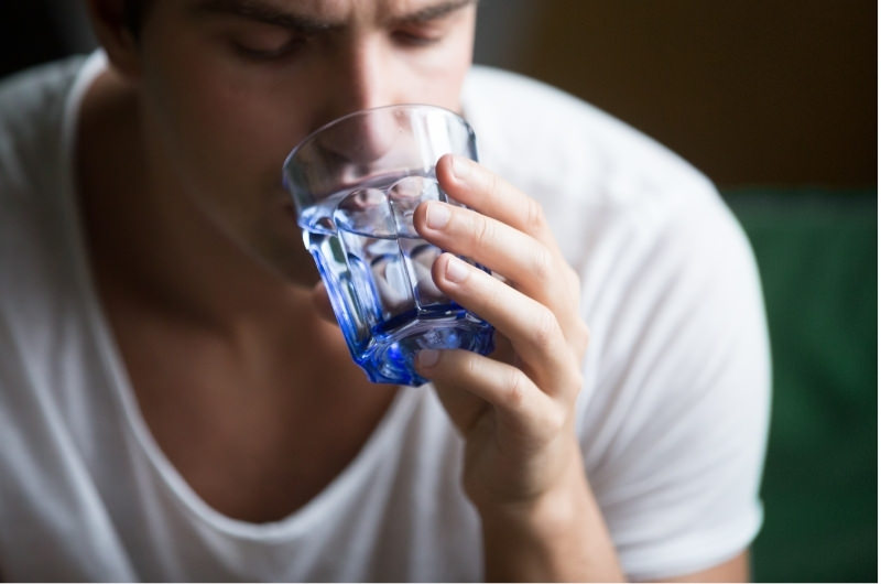 A young man is drinking water from a glass, wondering why it's tasting slightly sweet to him.
