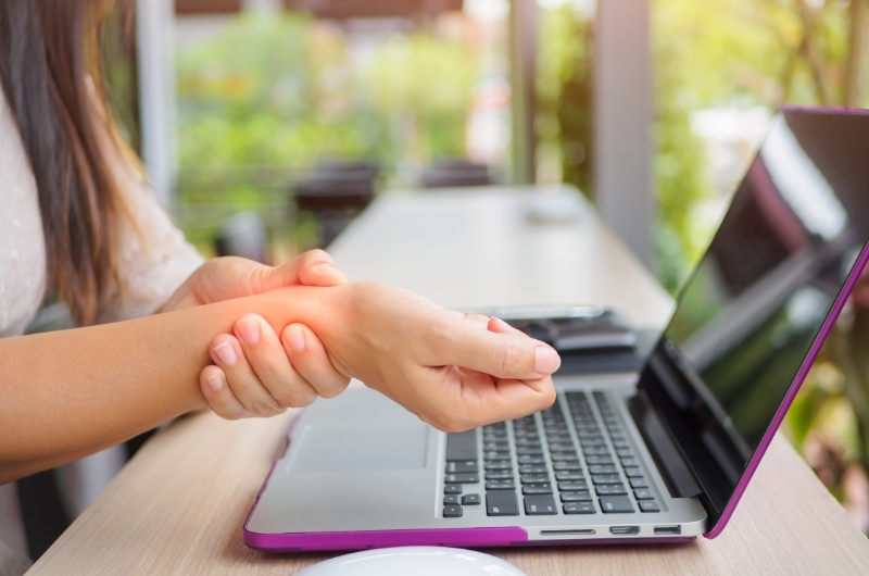 A young woman has wrist pain (possible carpal tunnel) because of heavy typing on her laptop.