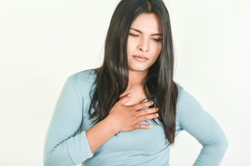 A woman is holding her chest after feeling pain in the area due to her acid reflux.
