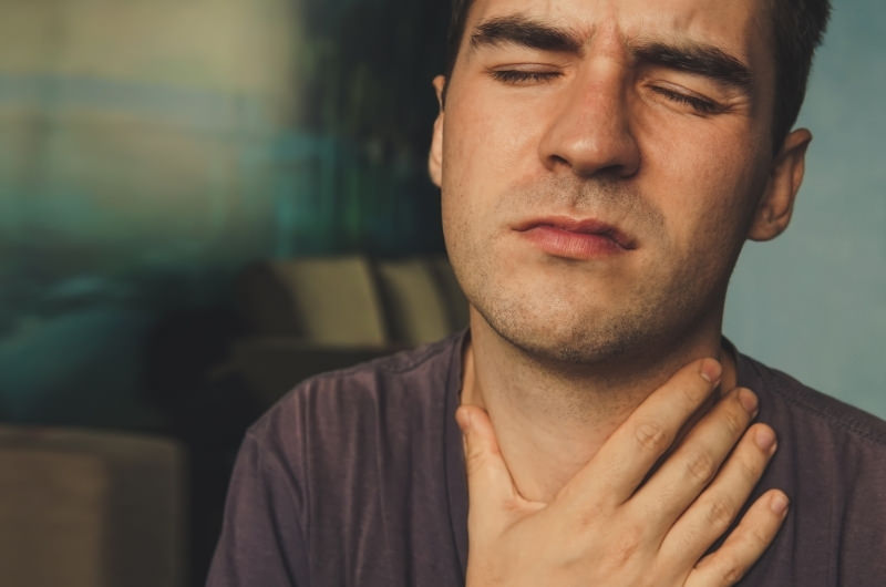 A young man is clenching his throat after feeling sharp pain by his Adam's Apple.