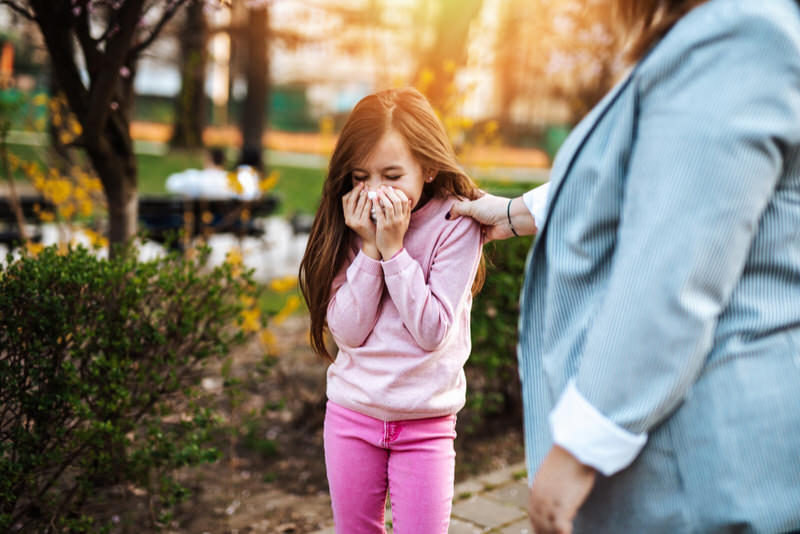 A little girl stopped walking at the park to blow her nose, which feels stuffy and blocked.