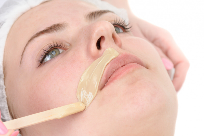 A young woman is waxing her upper lip area to remove hair.