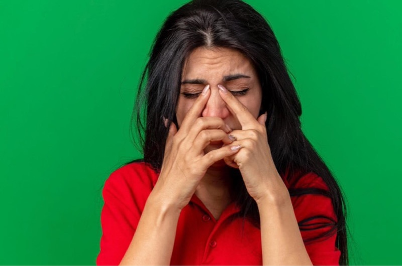 A young woman is clenching her nose as the pressure in it is causing her pain.