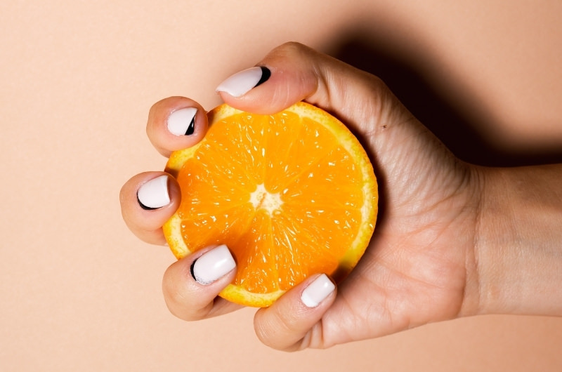 A woman is holding half of a navel orange, on that usually doesn't have any seeds.