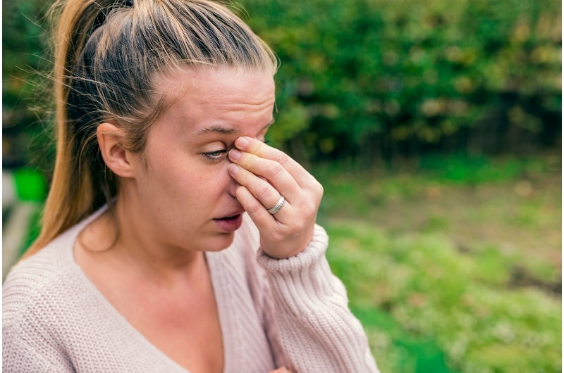 A woman is clenching the sides of her nose because she's having a headache along with sinus conditions.