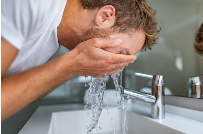 A man is rinsing his eyes with running water after he got some black pepper in his eyes.