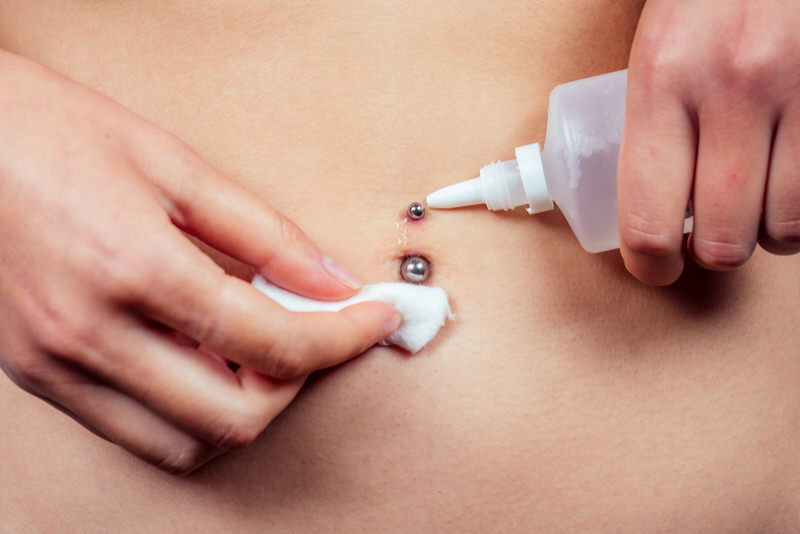 A young woman is disinfecting her new belly button piercing.