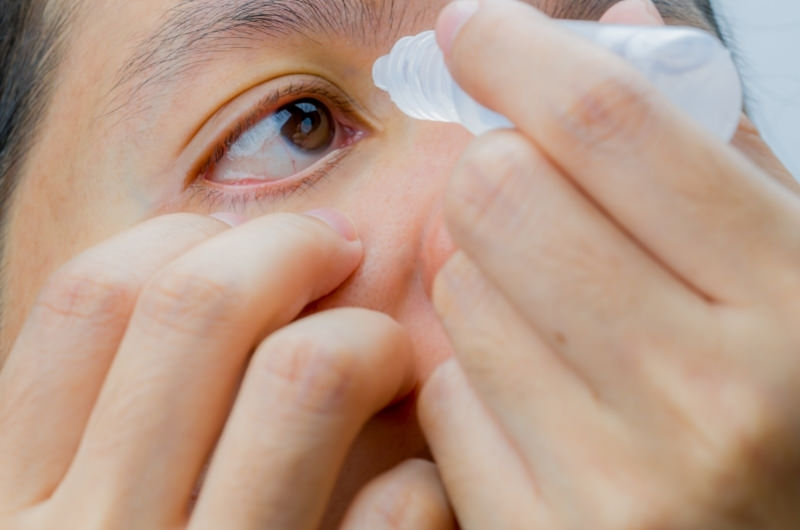A young man is using eye drops to help clear his eyes from some toothpaste that accidentally got in.