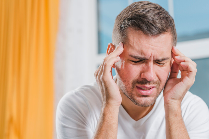 A man is touching his head as he's having a severe headache, a symptom of Cerebrospinal Fluid Leak.