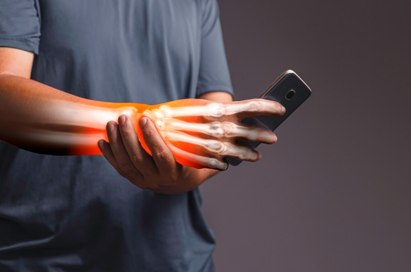 A graphic showing a man holding his phone but experiencing pain in his palm as a result of having carpal tunnel syndrome.