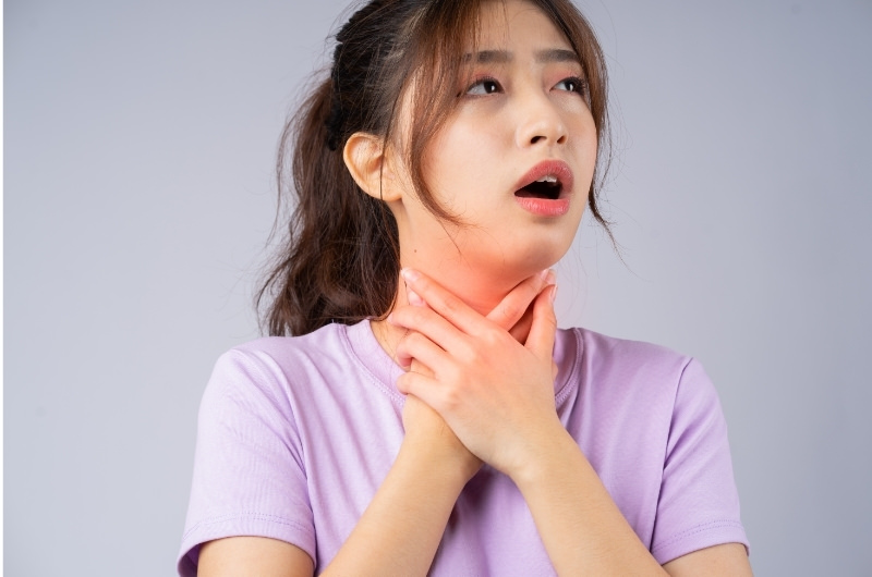 A young woman is having a burning sensation in her throat and is clenching her throat with both hands, she might have silent reflux.