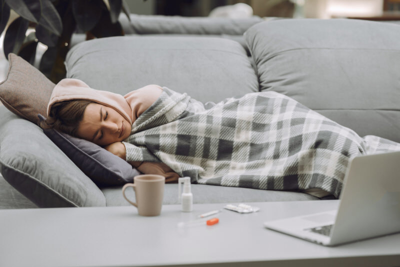 A woman with the cold is resting on the sofa after taking medicine to relieve her symptoms.
