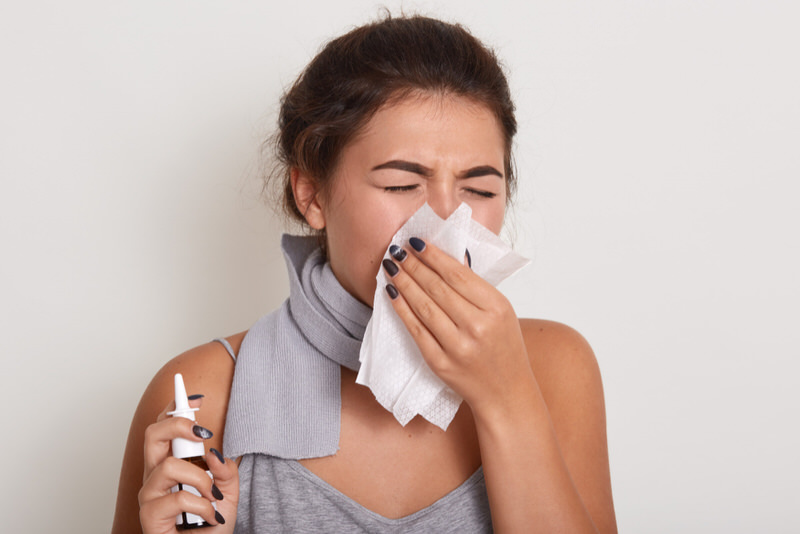 A woman is using a nasal spray to help with her sinus infection.