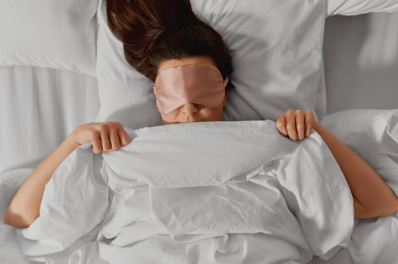 A woman is using a sleeping mask while sleeping in her bed so that the ceiling fan doesn't make her eyes dry overnight.