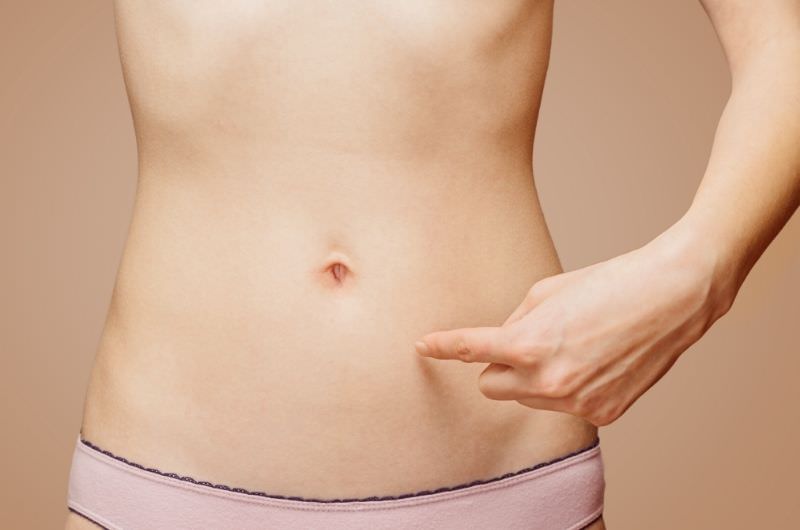 A woman is pointing her finger to a spot below her navel, which is a good pressure point area to help pain from relieve period cramps.
