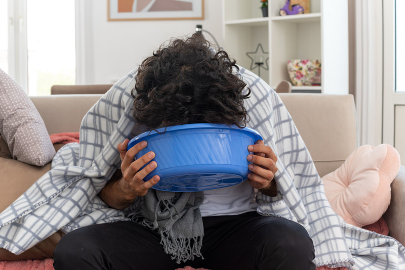 A man with a hangover is vomiting in a large container