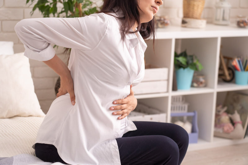 A pregnant woman is sitting down to rest her lower back pain.