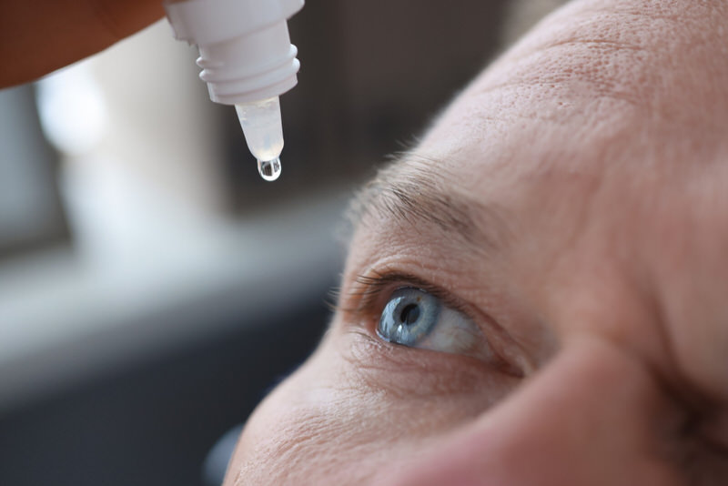 A man is putting eye drops in his eye for his glaucoma