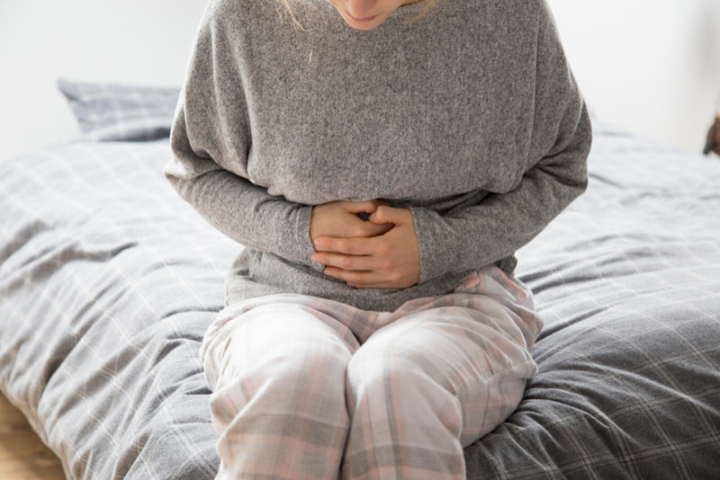 A woman with gastritis is sitting down because of pain she's feeling by her stomach