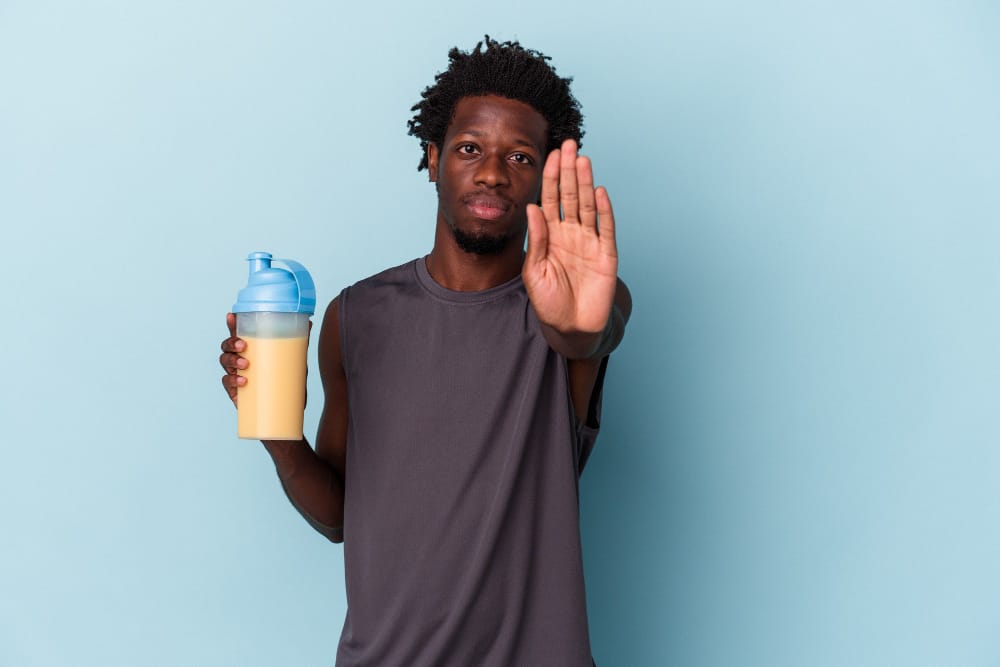 A young man is saying no to drinking his protein shake, because of the possible side effects