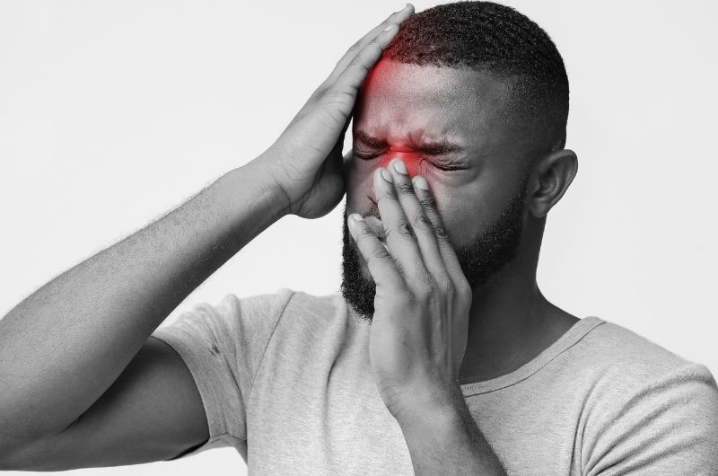 A man is holding his nose and head because of pain from his sinusitis