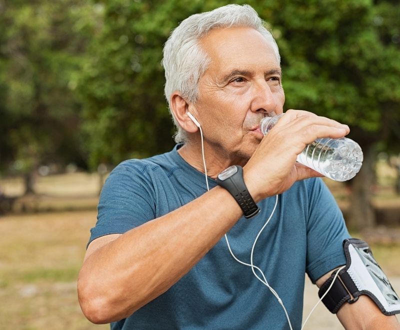 An older man is drinking plenty of water to stay hydrated as he runs