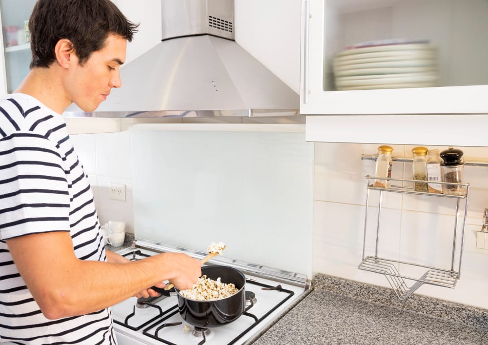 A young man is popping popcorn at home on the stovetop to enjoy the snack and prevent heartburn