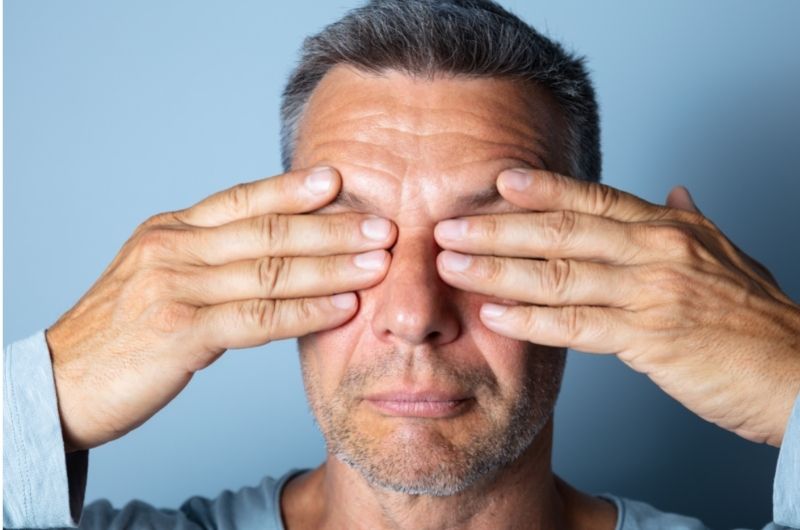 A man is massaging his eyelids to loosen any oils backed up in his eyelid oil glands, and prevent blepharitis.