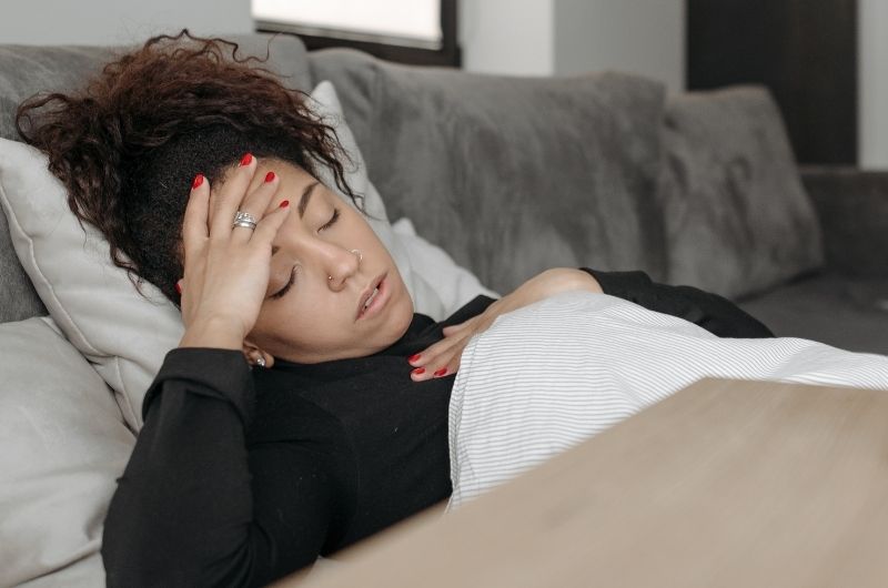 A young pregnant girl is laying down because she's experiencing morning sickness
