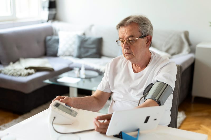 An older man is checking his blood pressure at home to monitor his heart health.