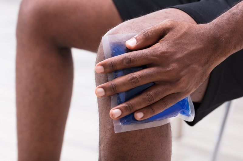 A man is using an ice pack on the side of his left knee, where he's having numbness pain