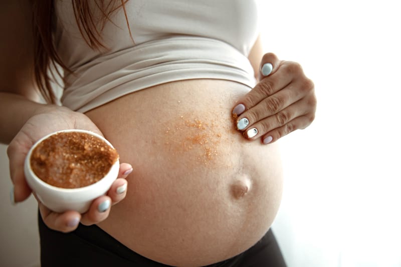 A pregnant woman is doing a sugar scrub on her belly to help exfoliate the skin and prevent stretch marks