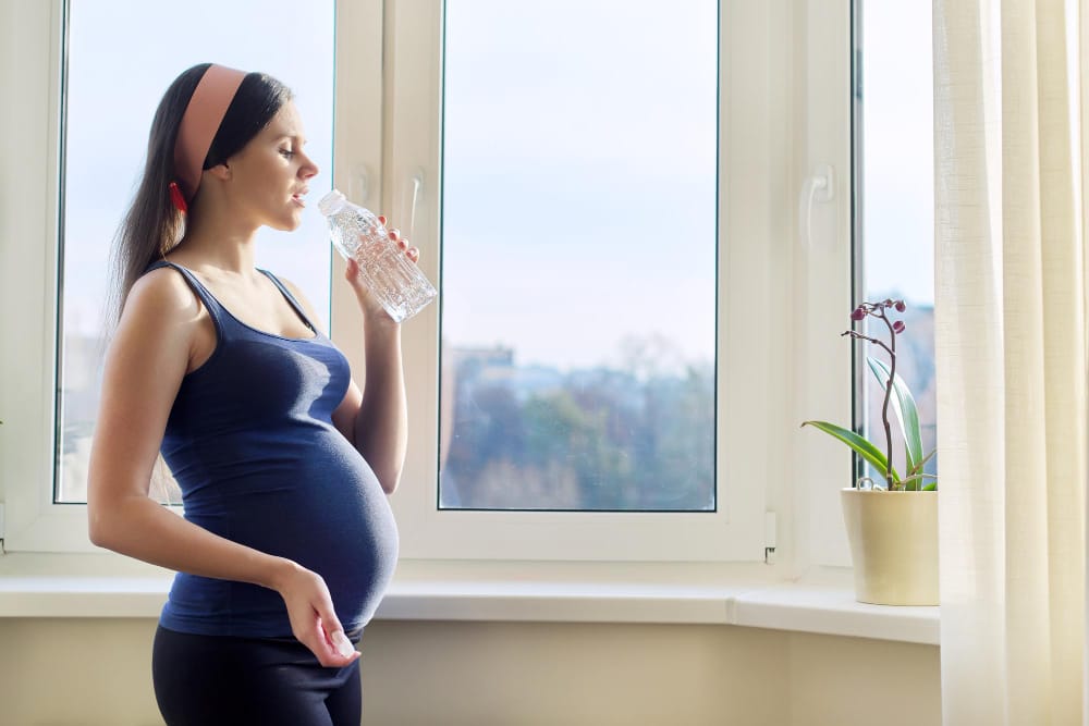 A young pregnant woman is drinking plenty of water to naturally help reduce her cold-like symptoms