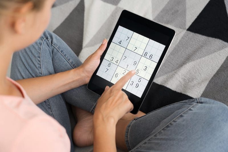 A young woman is playing Sudoku on her tablet as a daily brain exercise
